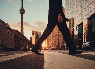 Man in suit crosses a street with CN Tower in the background