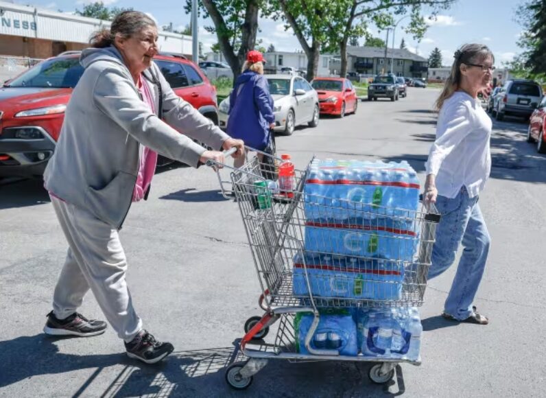 Leah Tabaldo, right, and Audrey Hopman wheel a cart filled with bottled water to their Calgary retirement home from an emergency supply provided by the city on June 7. Calgary has been cut off from more than half its water supply since June 5. (Jeff McIntosh//The Canadian Press)