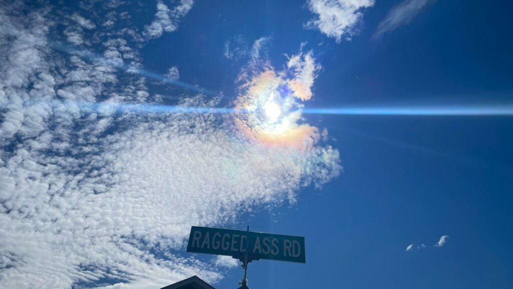 Ragged Ass Road street sign in front of a sunny sky