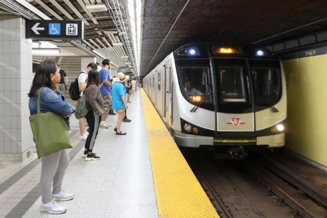 A subway train arrives at the Finch Station as people wait on a platform to board